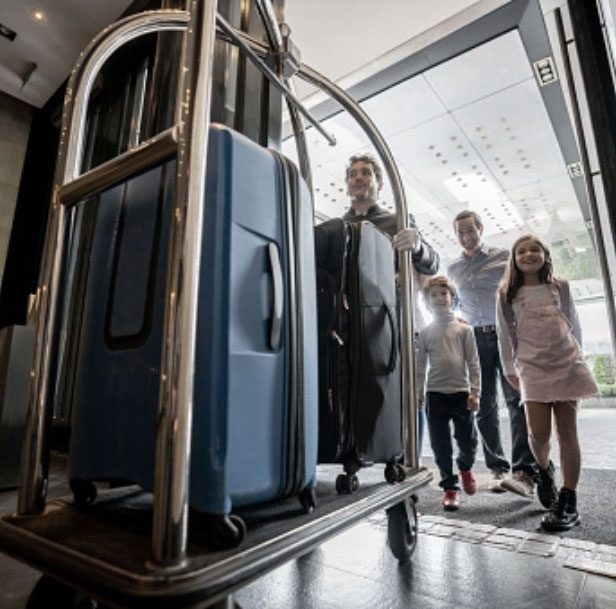 bellhop walking through hotel front door with family behind