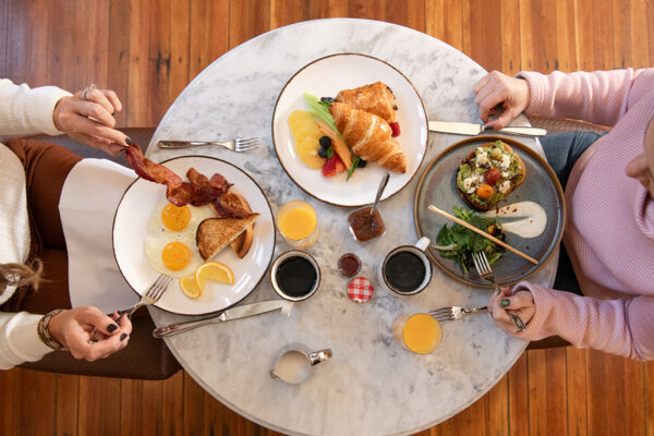 overhead view of two women at table with breakfast foods on plates, coffee and orange juice