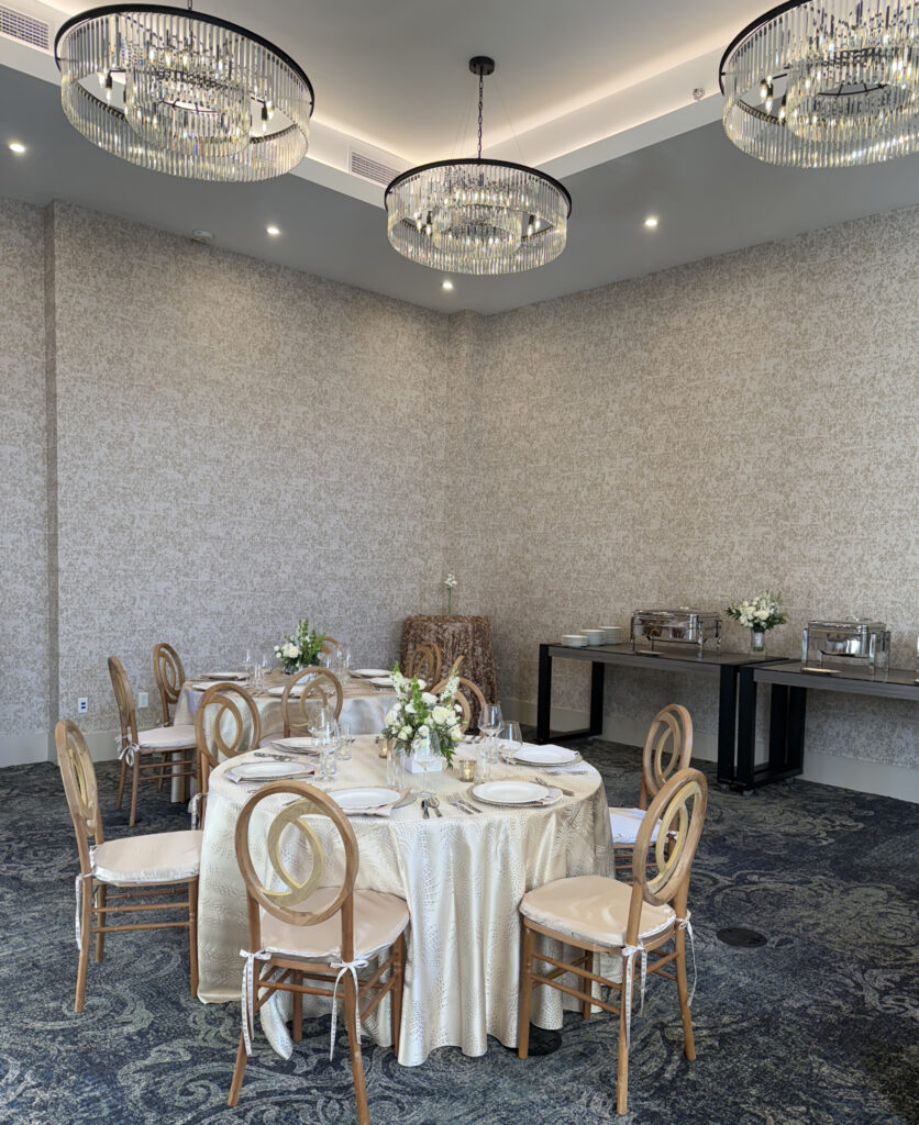 banquet space with tables, wood chairs, tall ceilings with chandeliers, gold wallpaper